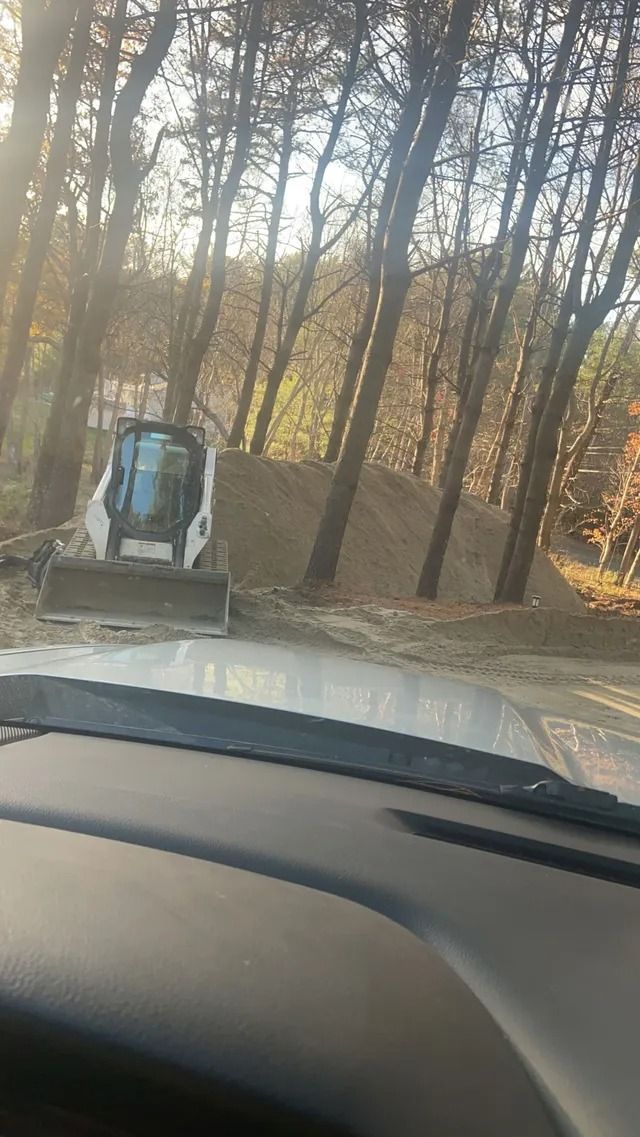 View through a car windshield of a dirt road in a wooded area, with a small vehicle ahead.