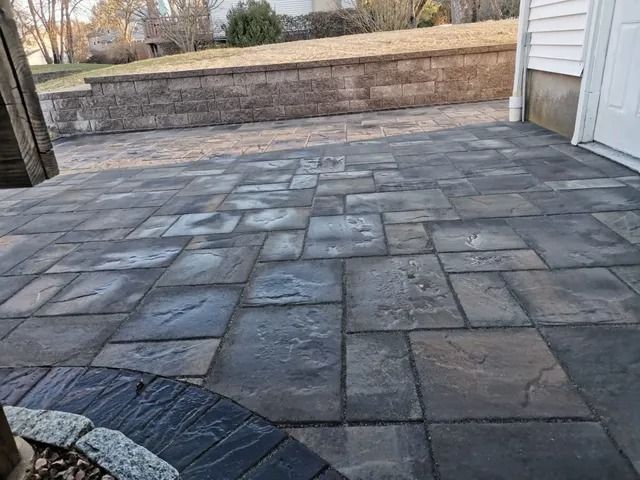 Stone patio with irregular gray pavers beside a white house and retaining wall.