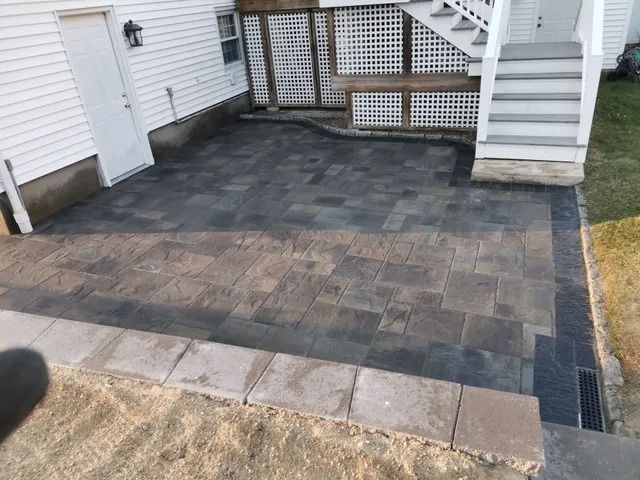 Backyard patio with dark pavers, steps, and white house siding