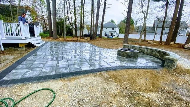 Backyard patio with gray pavers, circular fire pit, white deck, and trees by the water