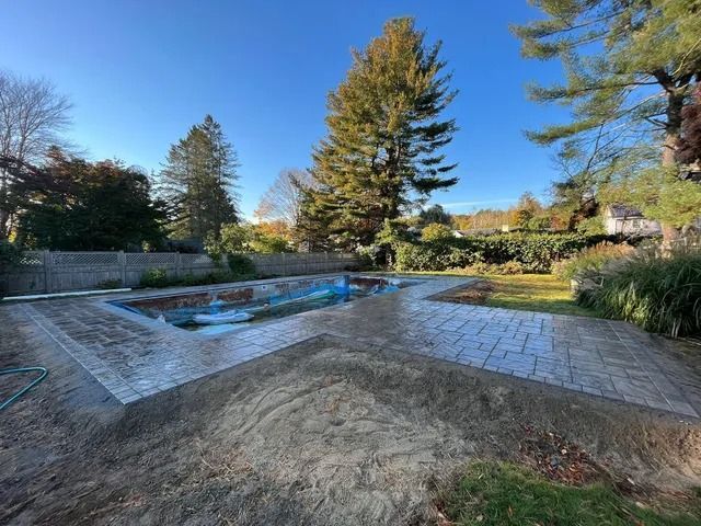 Empty backyard pool with a blue liner, stone patio, and trees under a clear sky