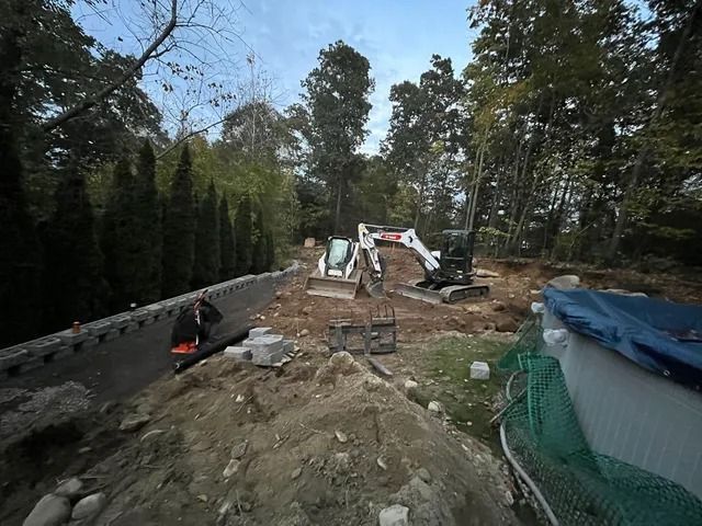 Construction site with excavator digging a backyard near a fence, trees, and a covered pool.