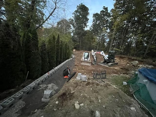 Backyard construction site with concrete wall, dirt piles, tools, and trees around the area