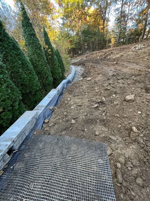 Steep dirt slope beside a narrow path with erosion control mesh and tall hedges in autumn.