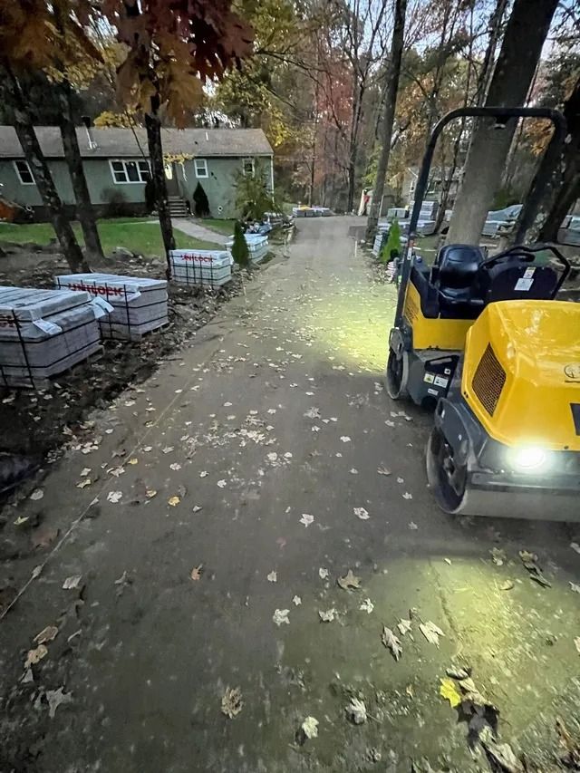 Tree-lined path with fallen leaves, houses on the left, and a yellow utility cart on the right at dusk