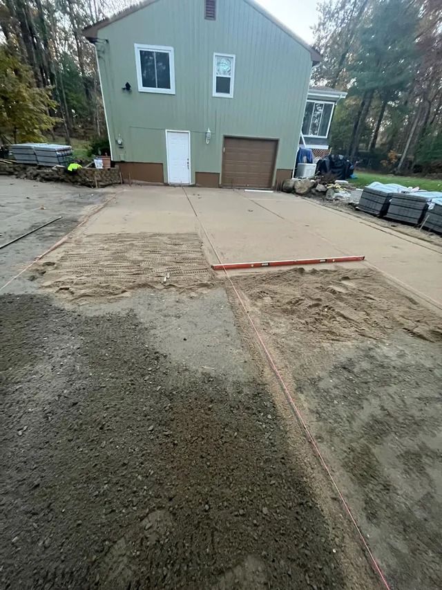 Driveway and garage under construction at a house, with unfinished concrete and dirt in the foreground.
