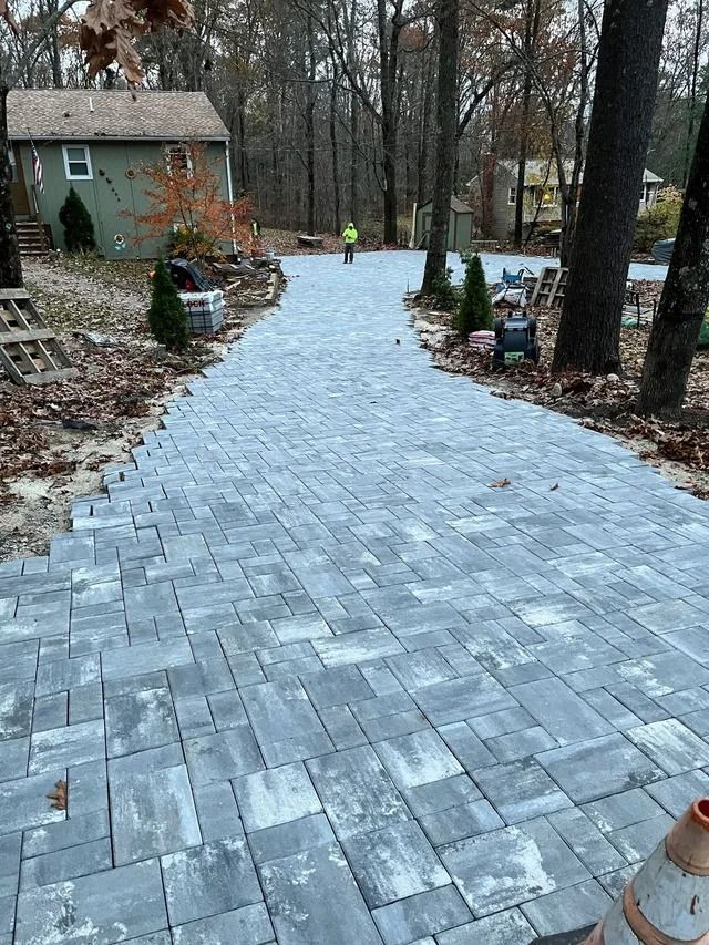 Snow-dusted stone walkway leading past a house and trees in a winter yard