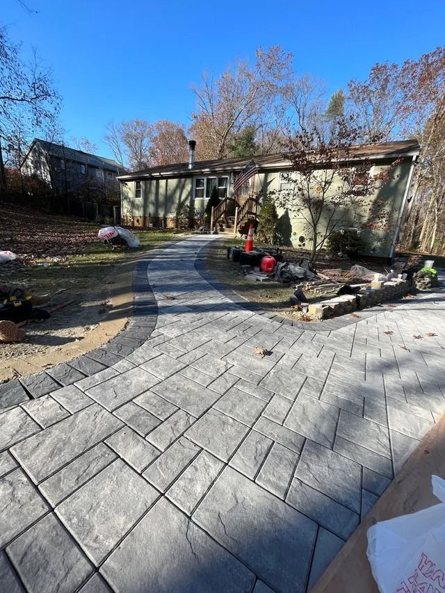 Backyard patio with gray pavers, pergola, fire pit, and trees under a clear blue sky