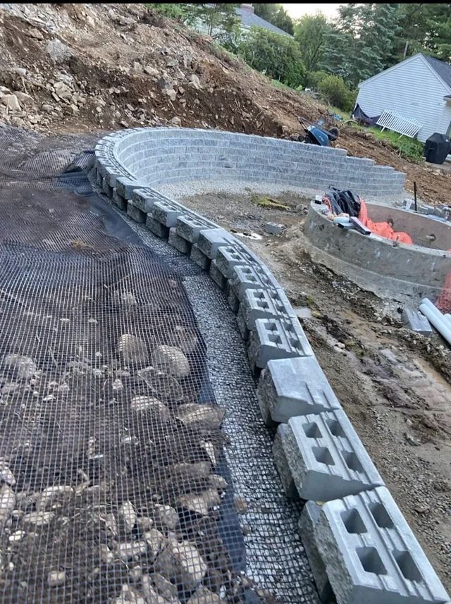 Curved cinder block foundation wall beside a gravel construction site with mesh ground cover and soil banks