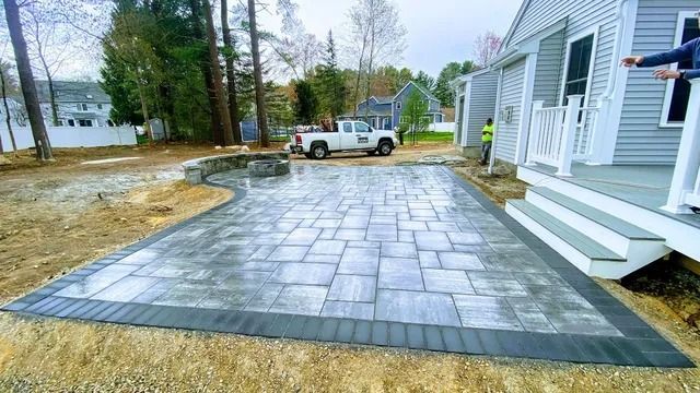 New stone paver patio beside a white house, with a curved border and a truck in the driveway