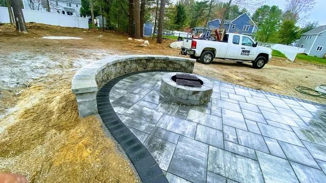 Curved stone patio with a circular fire pit beside a white pickup truck on a construction site