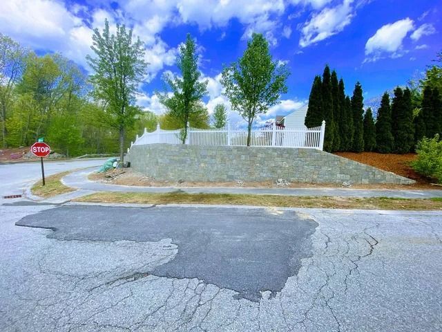 Stop sign beside a cracked road with a white fountain and tall trees under a bright blue sky