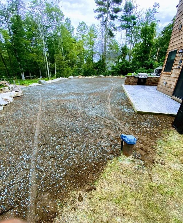 Gravel driveway beside a brick house, with trees and landscaping in the background