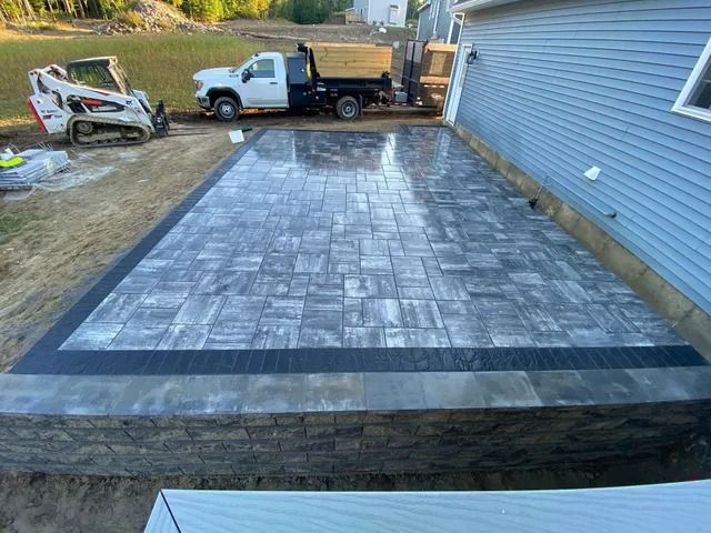 Backyard patio with gray pavers beside a blue house, viewed from the yard.