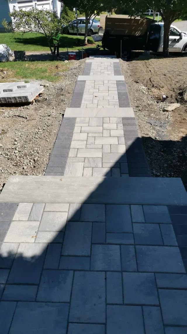 Gray paver walkway under construction leading through a yard, with dirt and stone borders