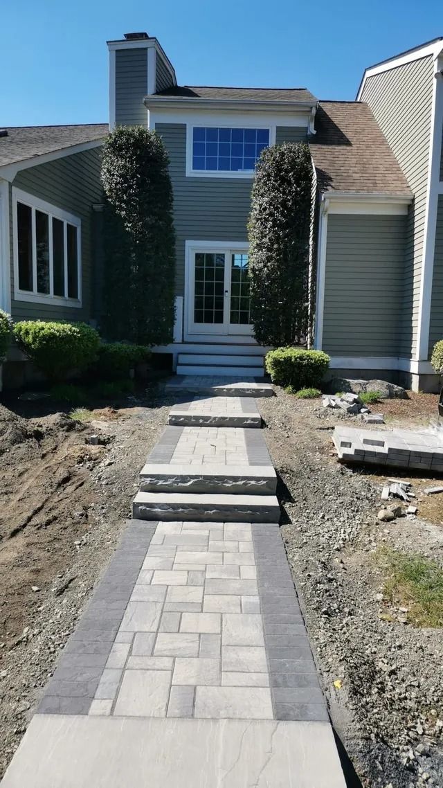 Front walkway of pavers leading to a house entrance with siding and boarded windows under construction.