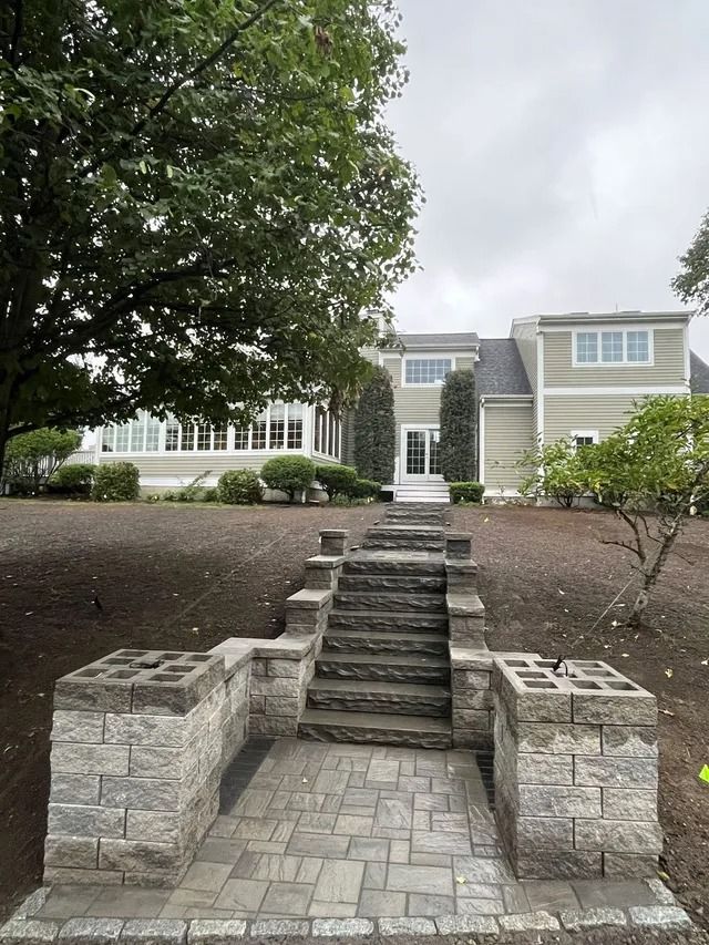 Front view of a house with stone steps, brick pathway, and large tree in the yard