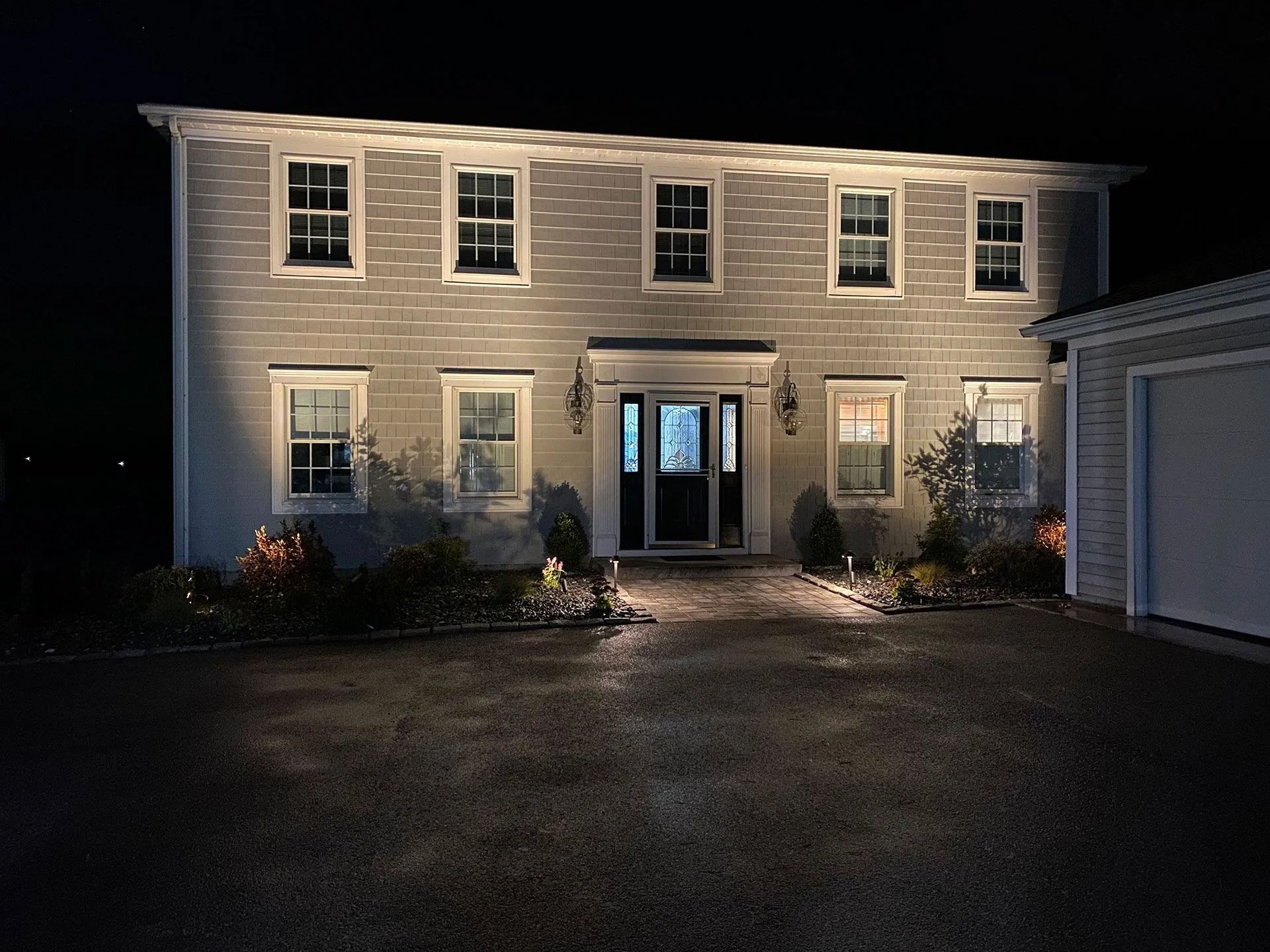 Nighttime front view of a two-story house with lit windows, a central front door, and a driveway in front.