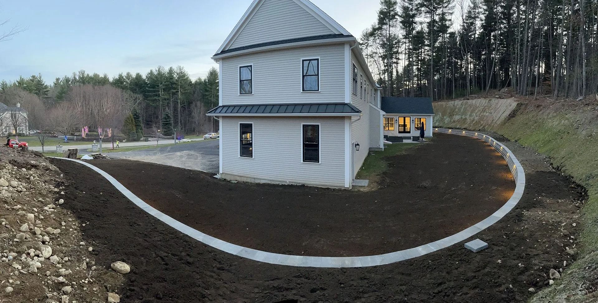 Small two-story gray house with a metal roof on a curved dirt path, surrounded by bare trees.