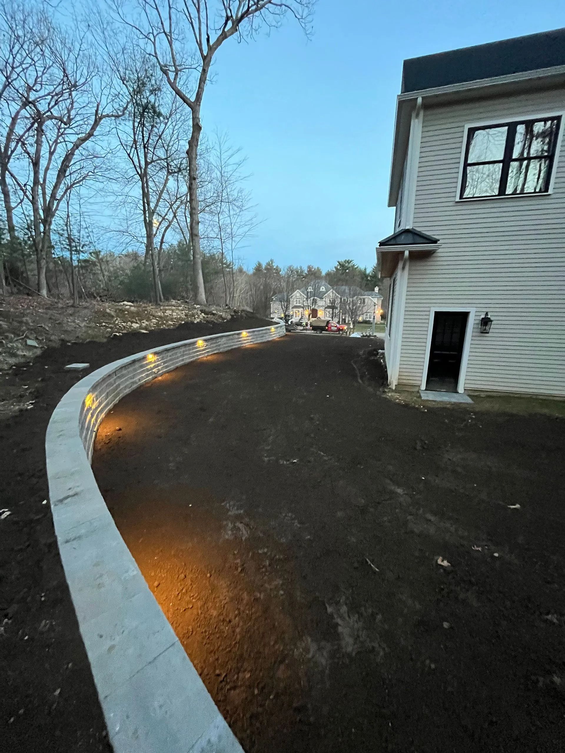 Curved driveway with glowing path lights beside a white house at dusk