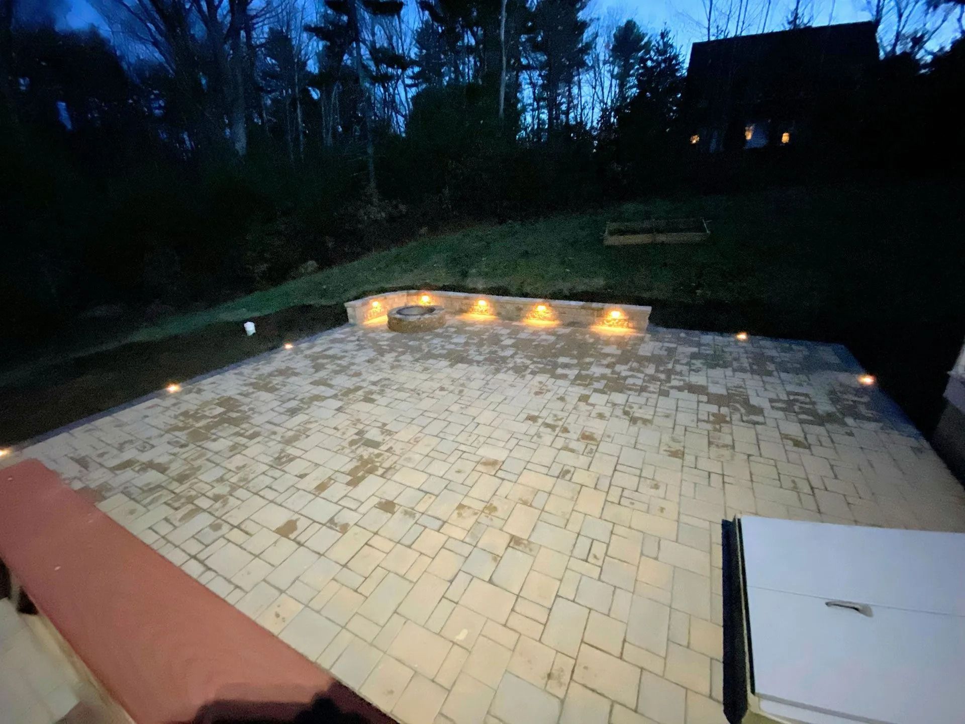Nighttime patio with lit built-in fire pit, tiled ground, and surrounding trees