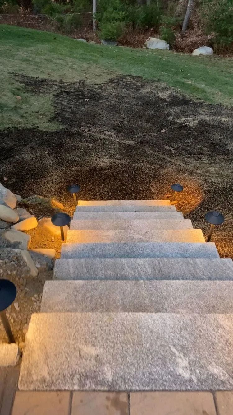 Outdoor stone steps lit by warm lights, descending to a grassy yard at dusk.