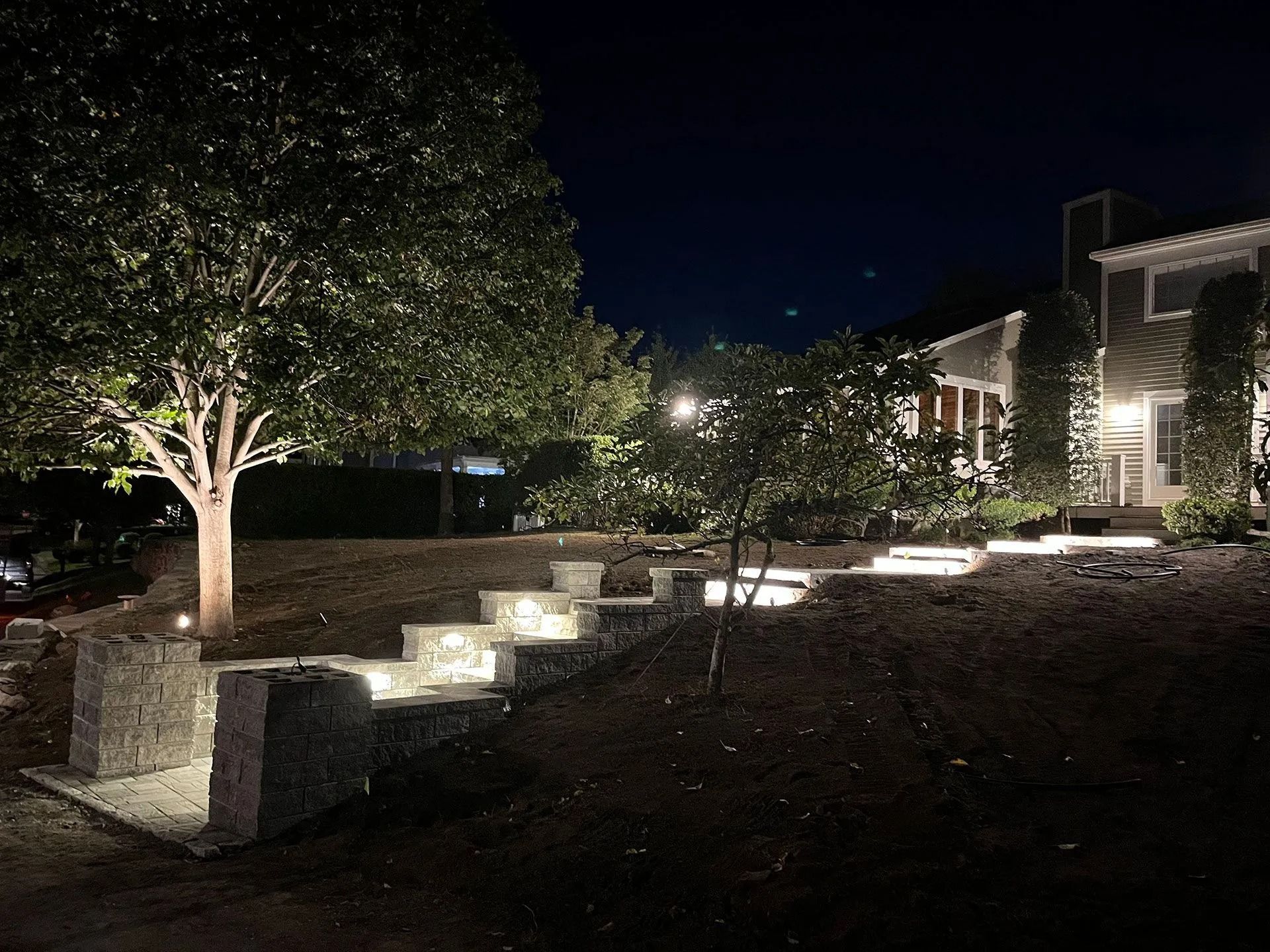 Nighttime landscaped walkway with lit steps, trees, and a building in the background