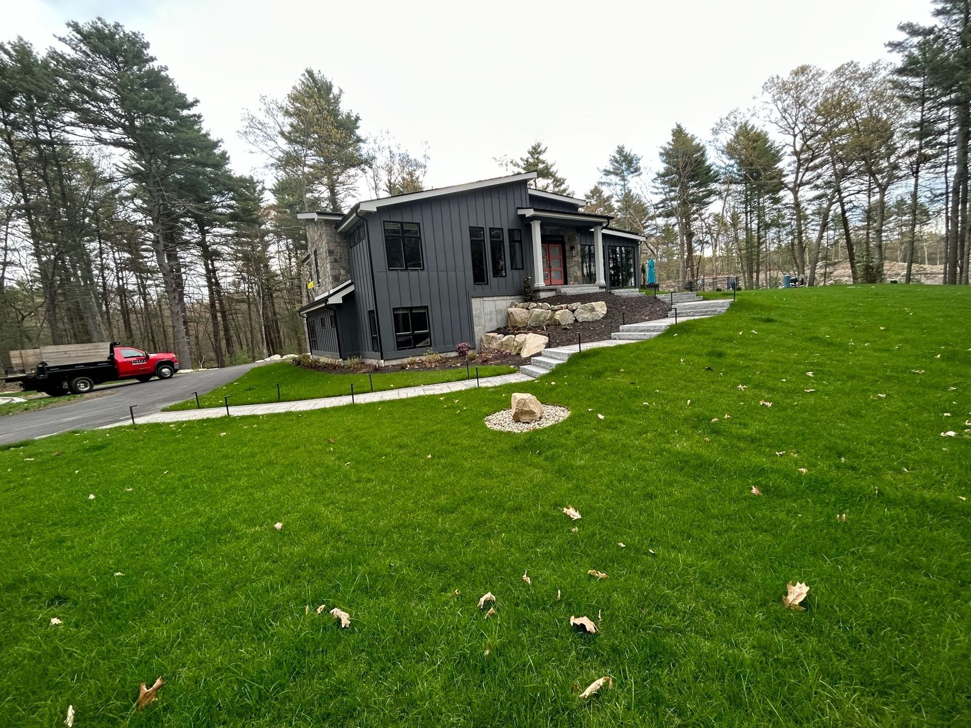 Modern dark gray house with a large green lawn and trees, viewed from the yard