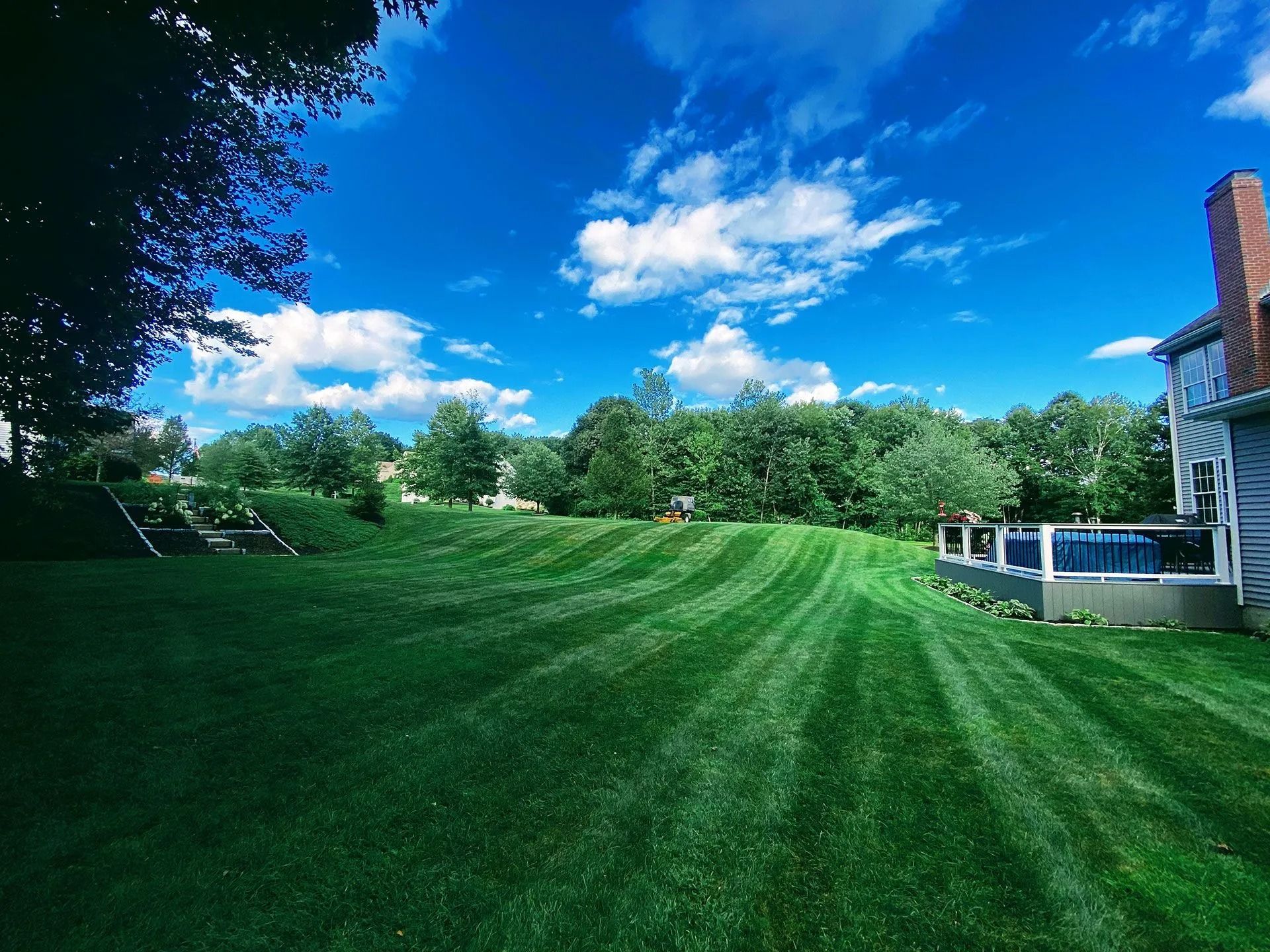 Bright green lawn beside a house under a vivid blue sky with scattered clouds