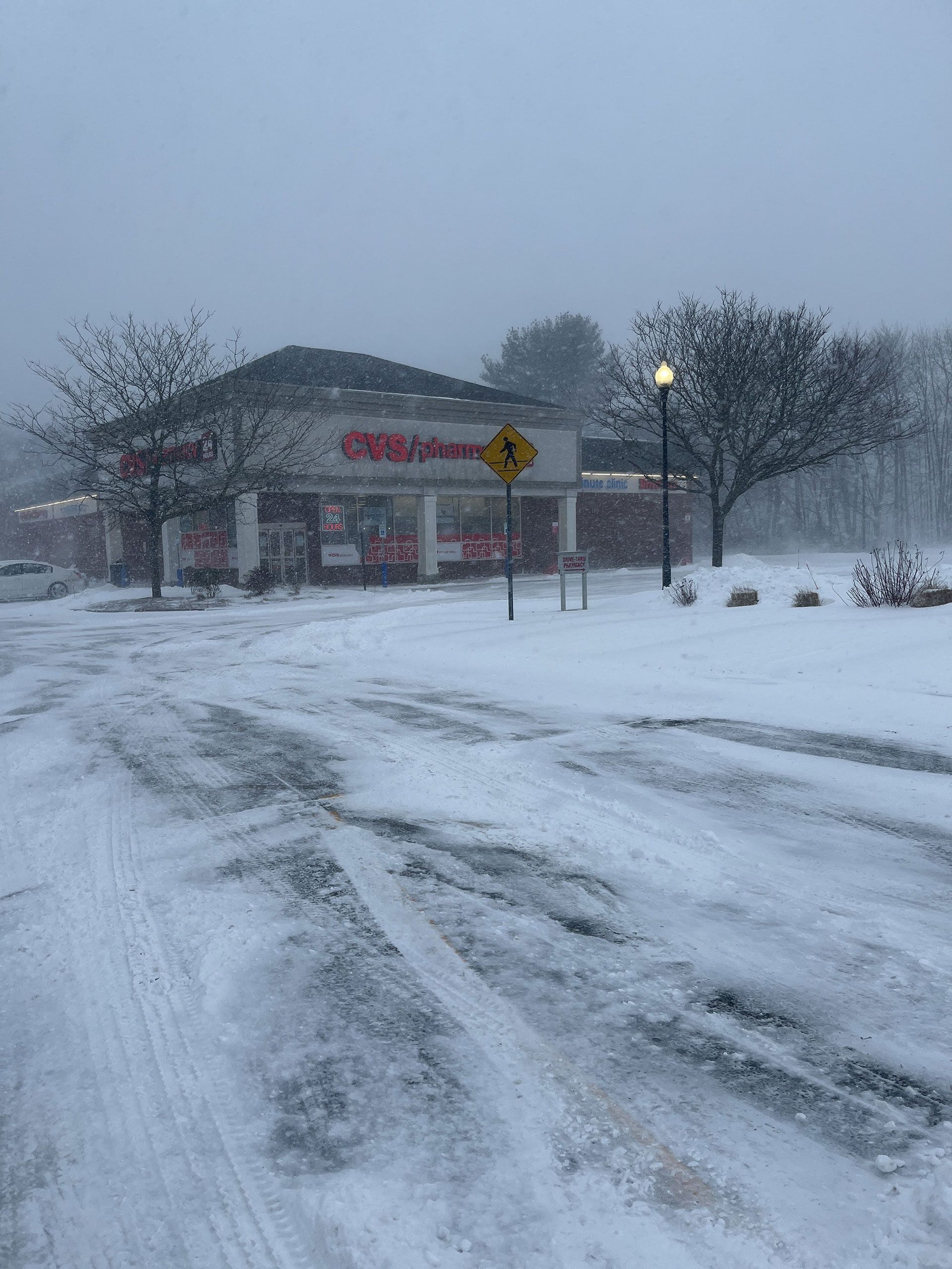 Snowy roadside view of a building and parking lot with deep tire tracks and a lit streetlamp