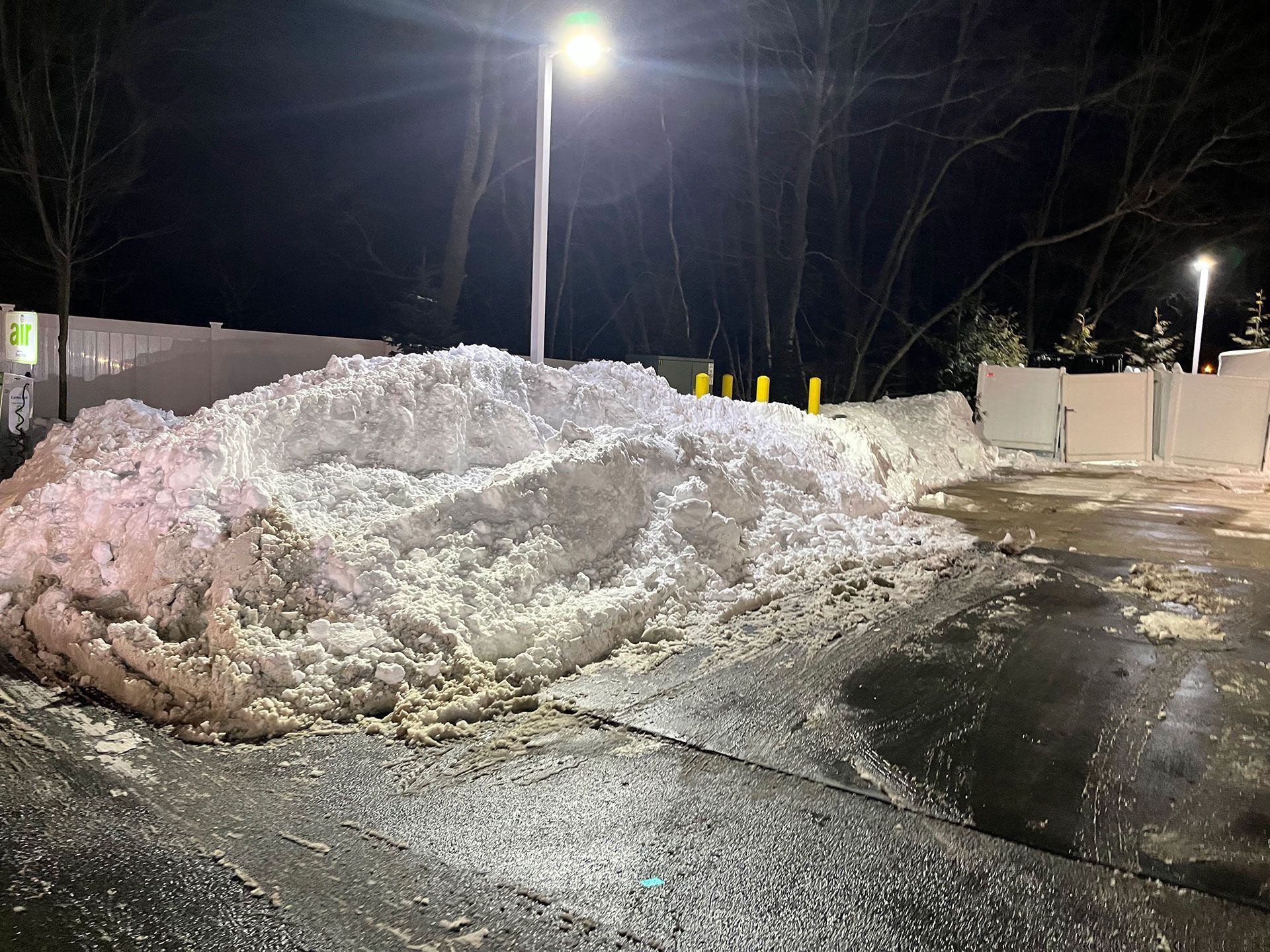 Large dirty snow pile in a wet, dark parking lot under bright streetlights at night