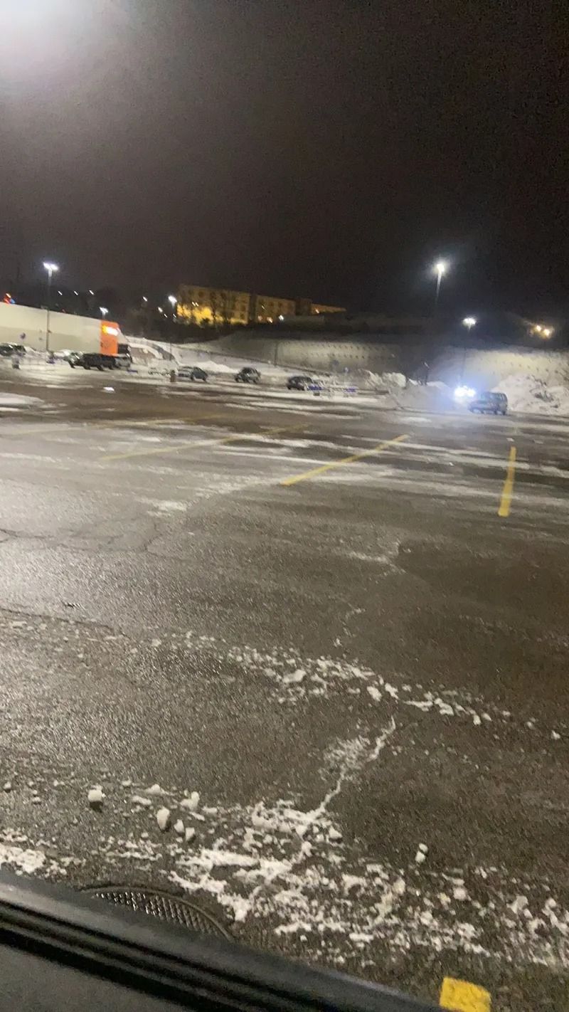 Snowy parking lot at night with icy pavement and distant building lights