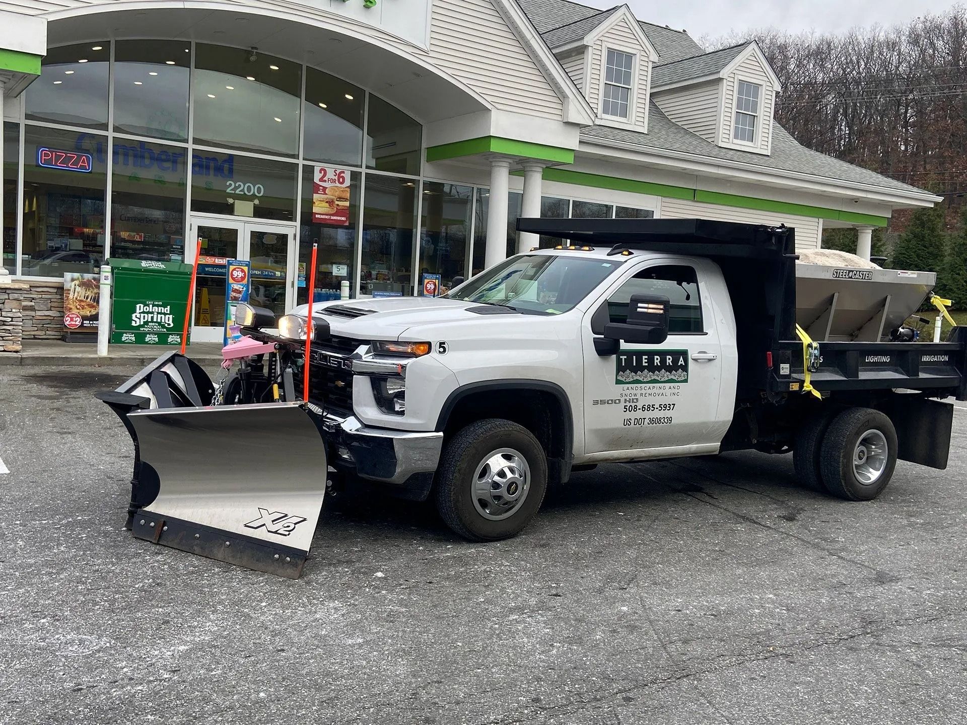 White utility truck with snowplow parked outside a store with glass storefront and gravel lot