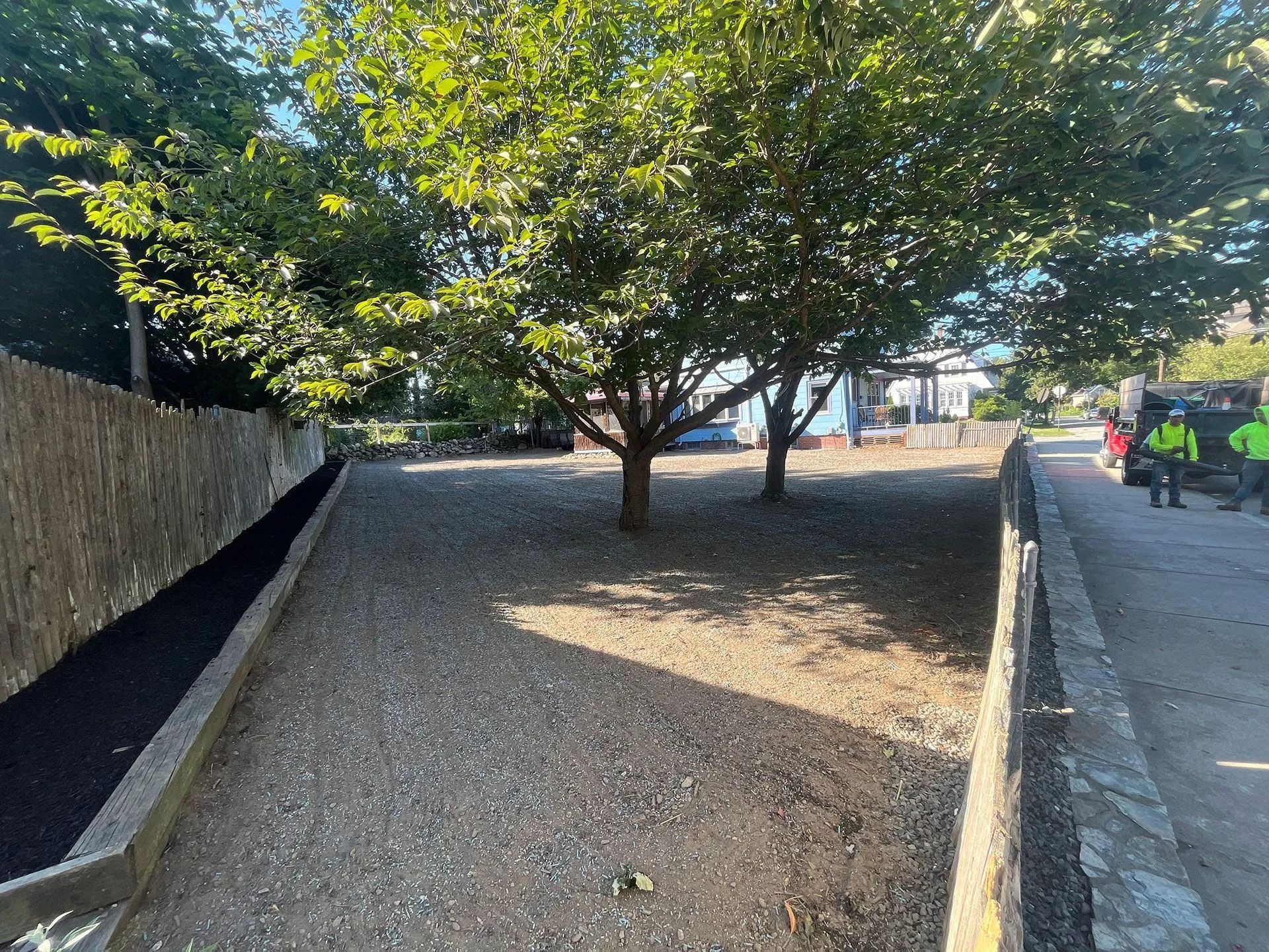Tree in a gravel-lined park path between walls, with a person in red on the right.