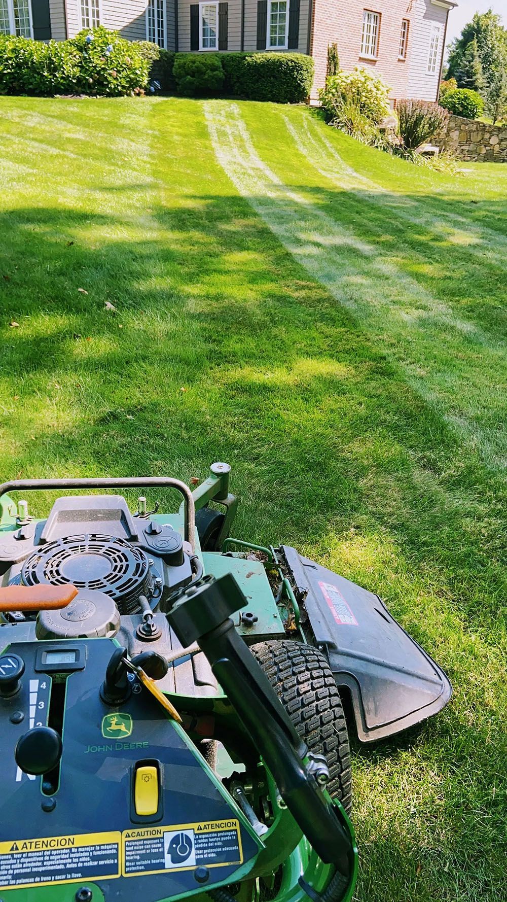 Lawn mower cutting striped green grass in a sunny suburban yard near a house