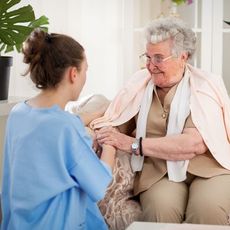 A nurse is talking to an elderly woman who is sitting on a couch