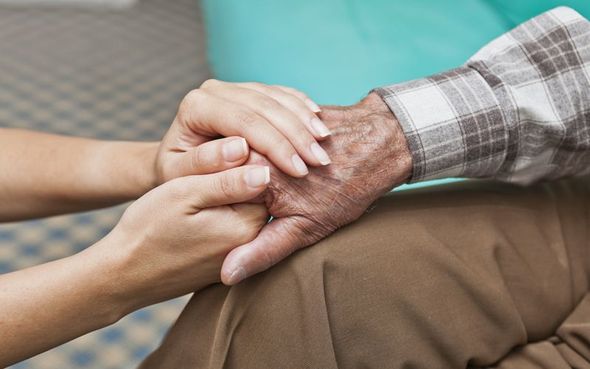 A man is talking to an elderly woman in a wheelchair while holding a cup of coffee.