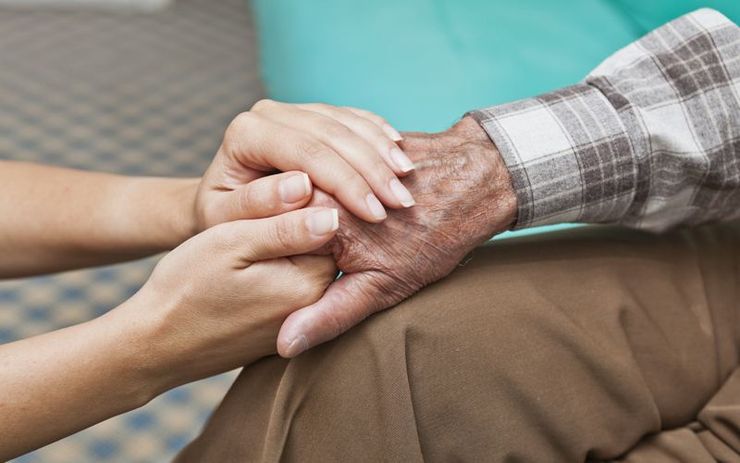 A man is talking to an elderly woman in a wheelchair while holding a cup of coffee.