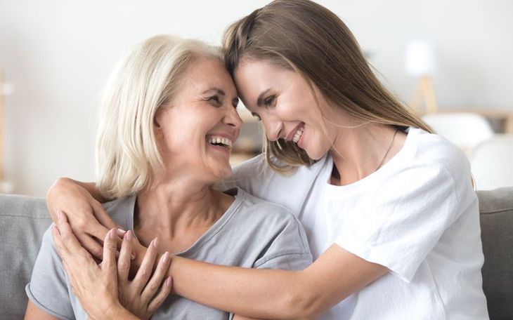 A young woman is hugging an older woman on a couch.