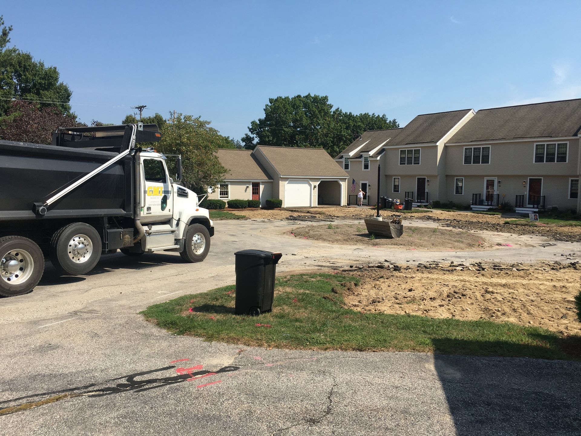 Dump truck parked at a construction site with townhouses in the background. Paved road and exposed dirt.