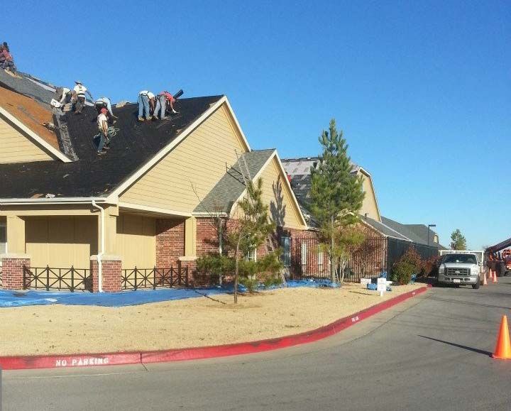 Roofers working on a residential roof, sunny day, with a truck and orange cone on a street.