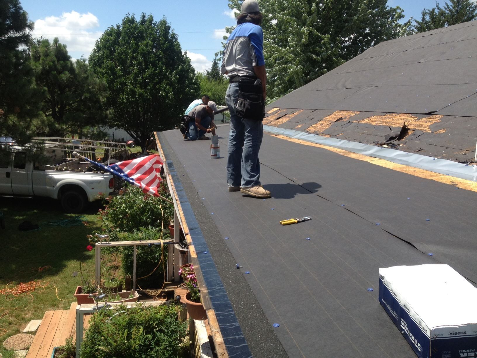 Roofers installing roofing material on a residential roof, sunny day.