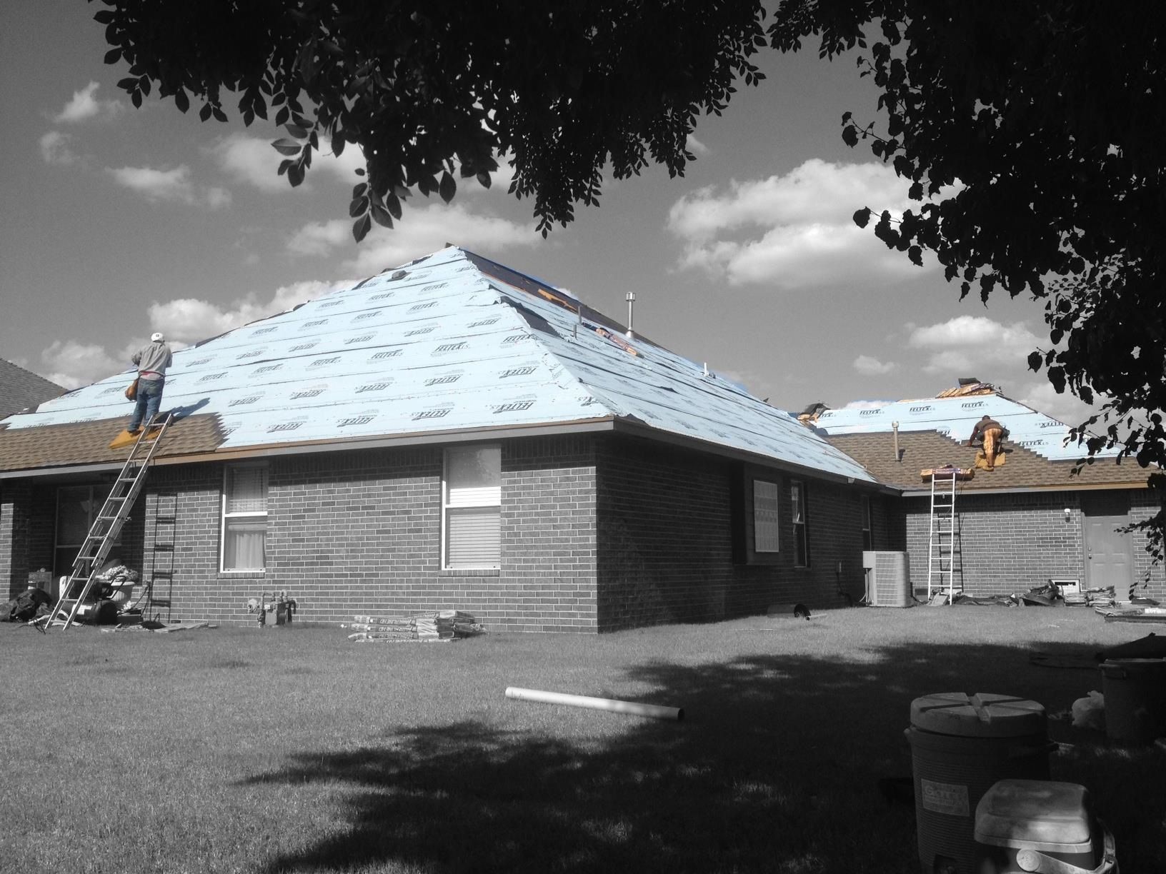 Roofers working on a house, placing blue underlayment on roof. Black and white photo with blue roof.