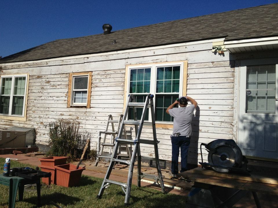 Exterior house renovation with a man working on a window frame, ladders, and a circular saw.