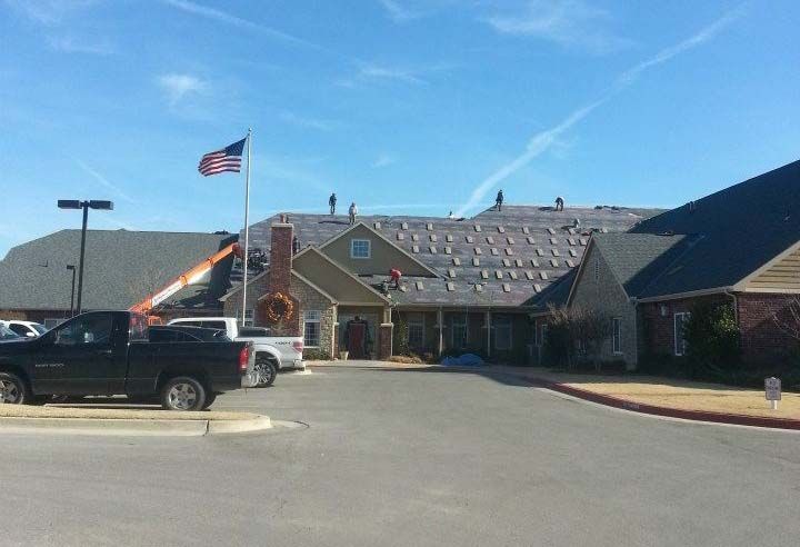 Workers on a roof with an American flag, black trucks, and a lift. Building being worked on.