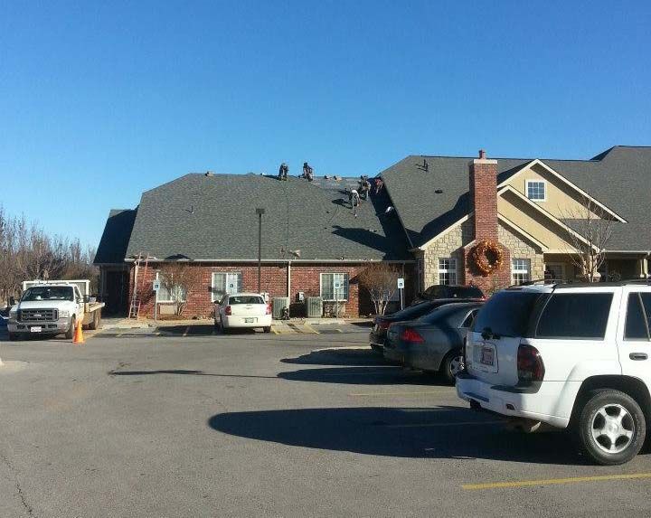 Roofers on a commercial building roof with a truck and cars in the parking lot on a sunny day.