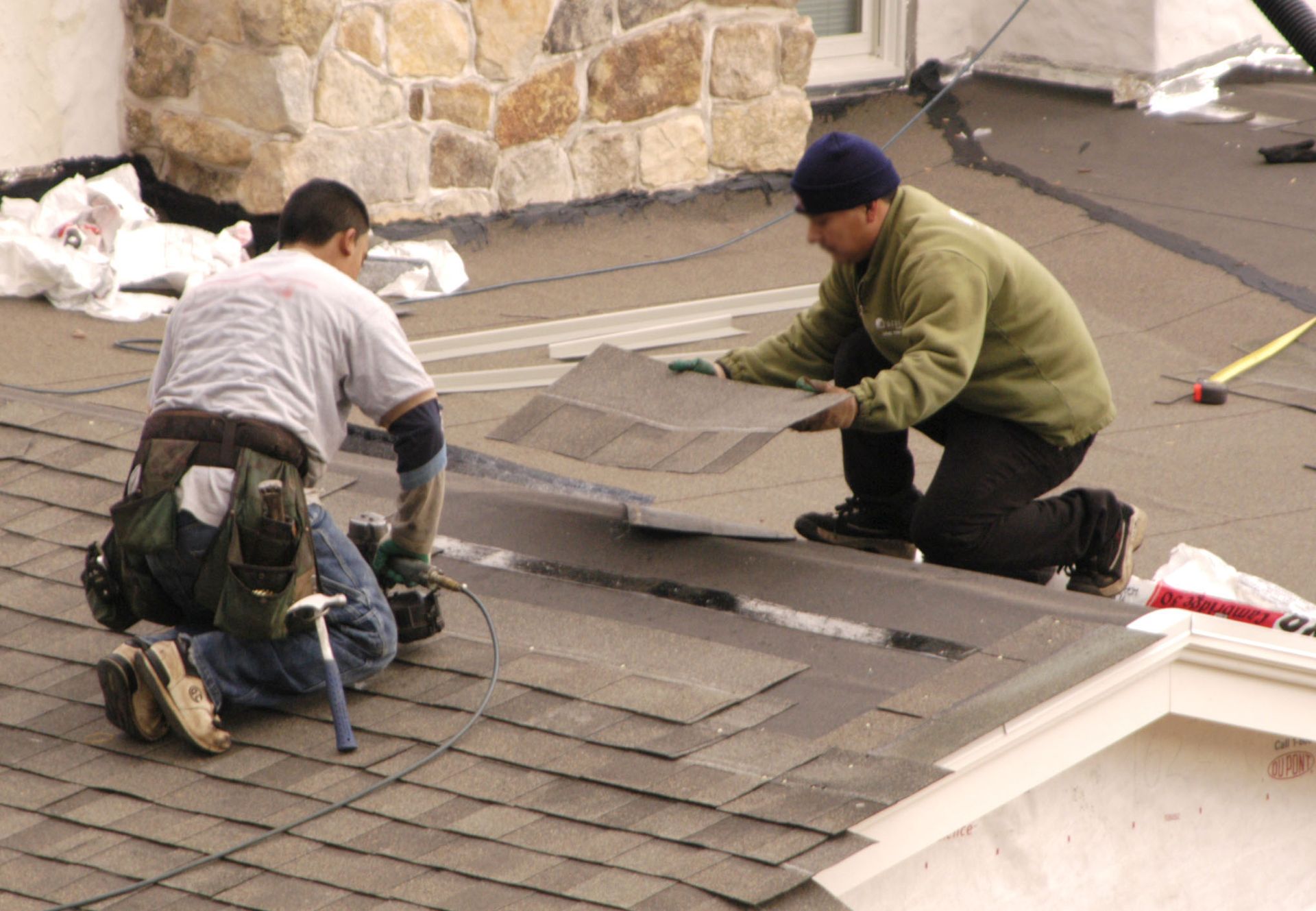 Two roofers installing asphalt shingles on a roof.
