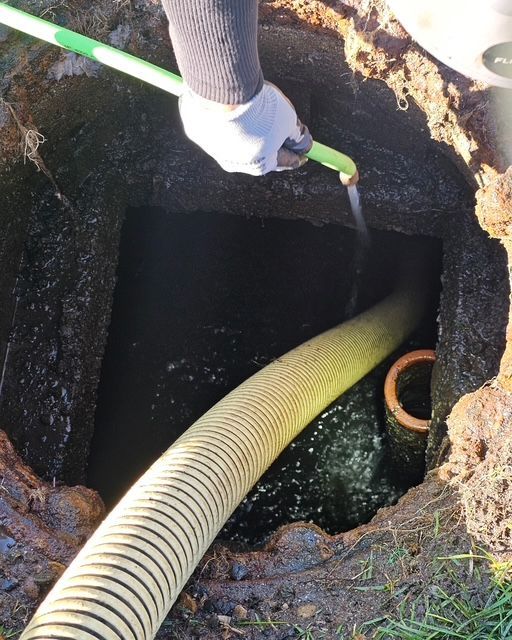 Person wearing gloves uses a hose to pump liquid from a septic tank.