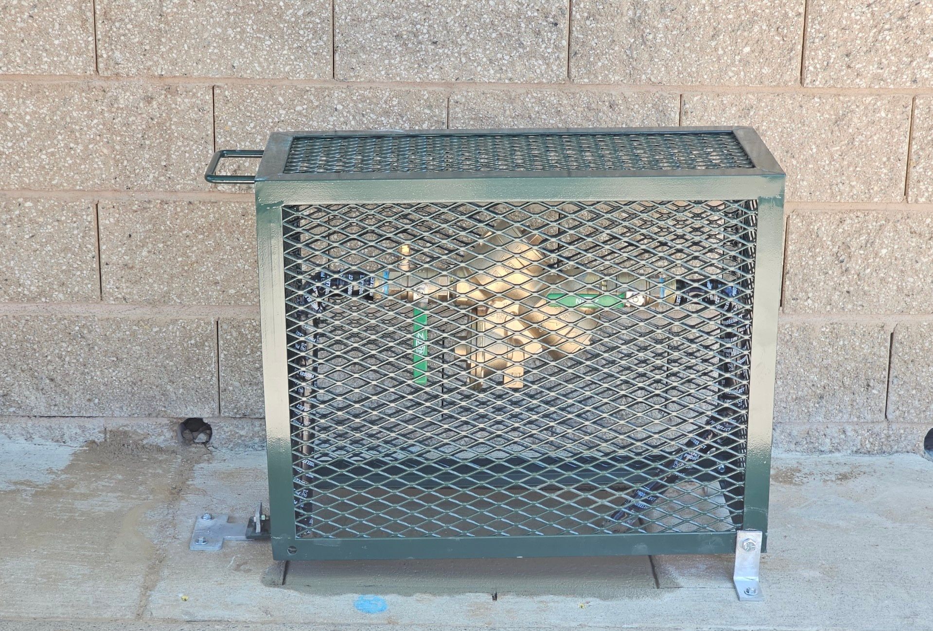 Green metal cage enclosing outdoor water pipes against a brick wall.