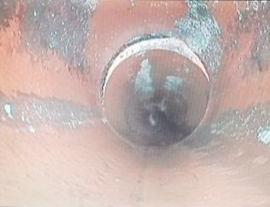 Inside a pipe, looking towards a round opening, with water and rust-colored walls.